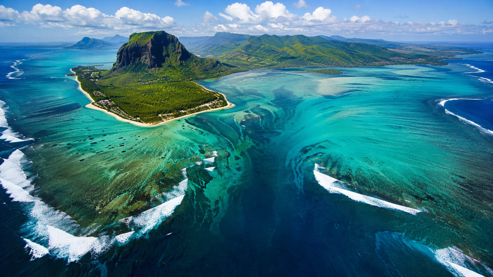 An aerial view of the famous Mauritius underwater waterfall illusion, where turquoise lagoons, coral reefs, and swirling underwater sand create the appearance of a giant waterfall flowing into the deep Indian Ocean.