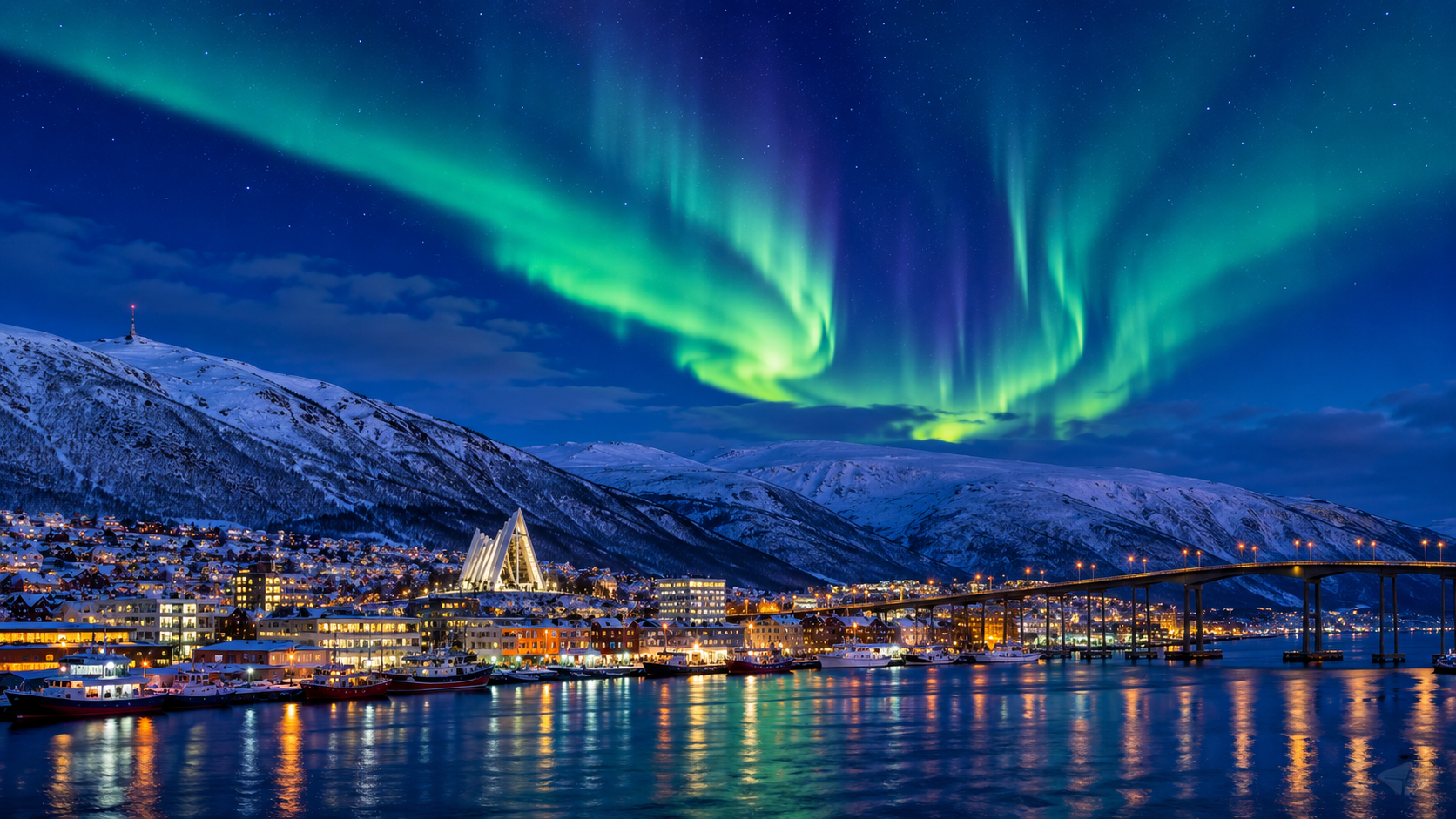 A breathtaking winter view of Tromsø, Norway, with warmly lit homes beneath a deep blue Polar Night sky as vibrant green Northern Lights dance above snow-covered mountains and the Arctic harbor.